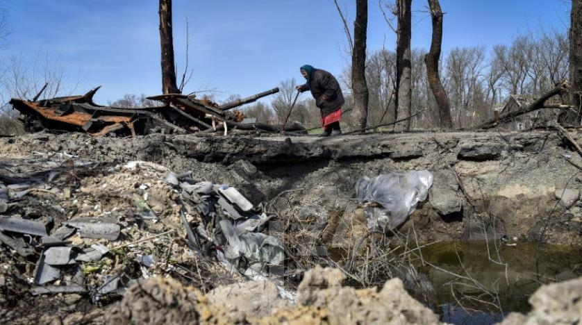 سيدة تمر بجانب حفرة خلفها انفجار قنبلة جوية على طريق في شمال كييف
