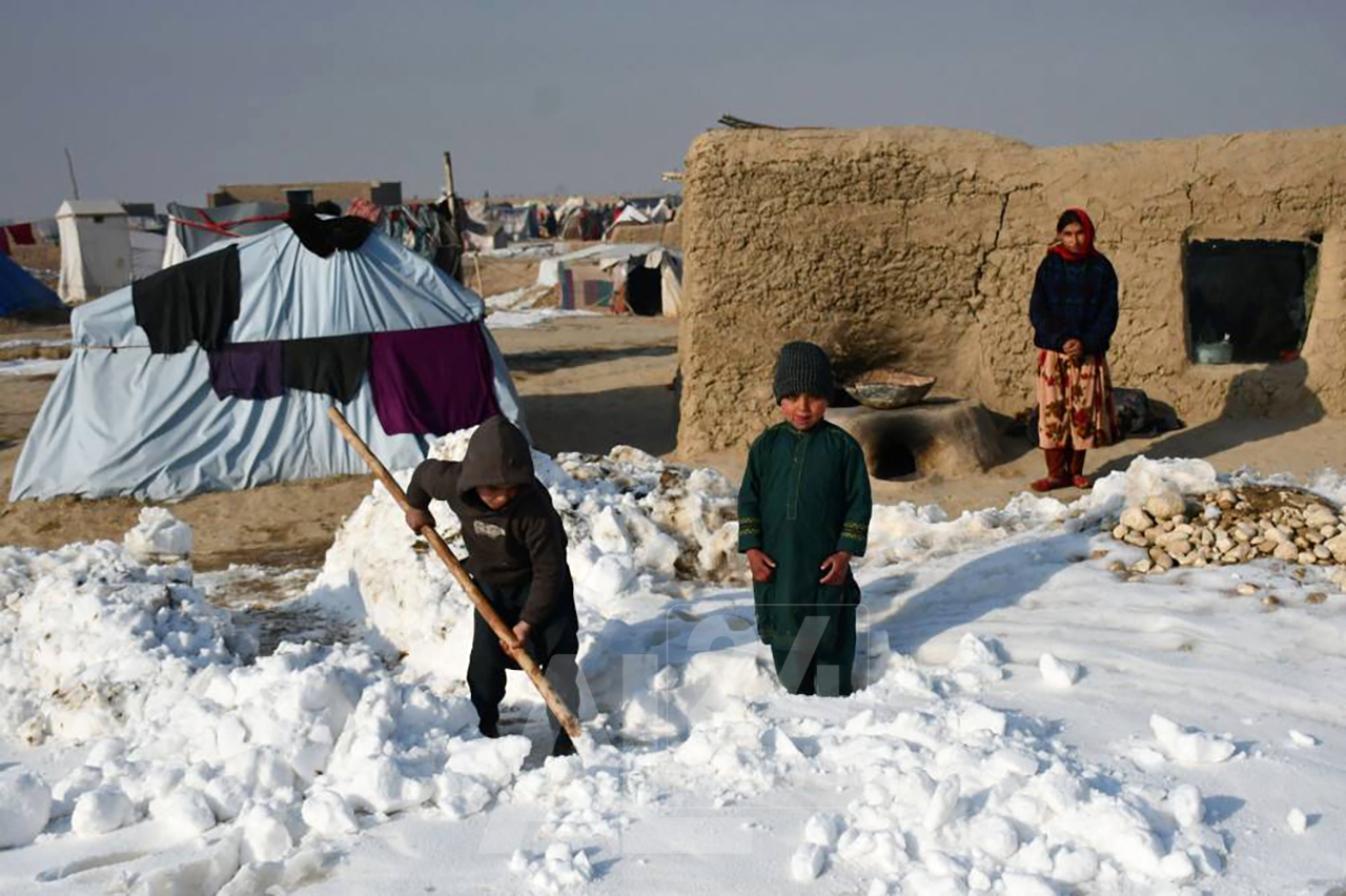 Afghan internally-displaced children shovel snow near their tents during a cold winter day at Nahr-e Shah-e- district of Balkh Province, near Mazar-i-Sharif on January 17, 2023. (Photo by Atif ARYAN / AFP)